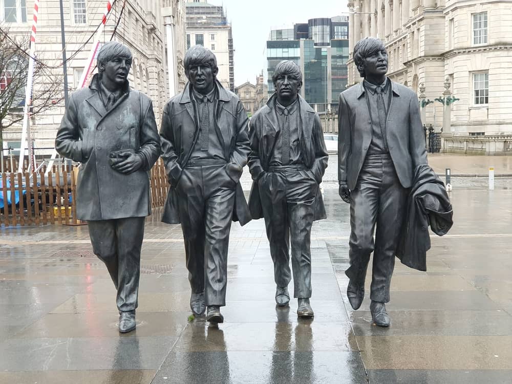 Famous band statues, city backdrop, rain.