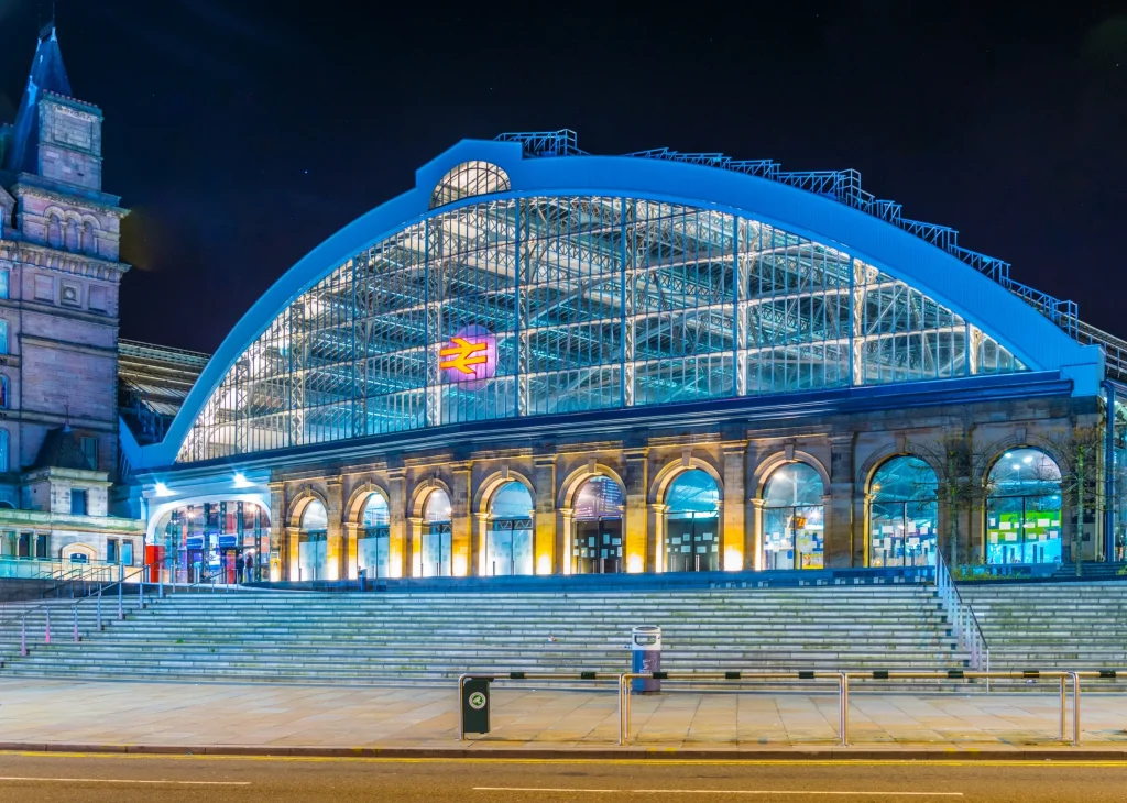 Glass-roofed train station, illuminated, night.